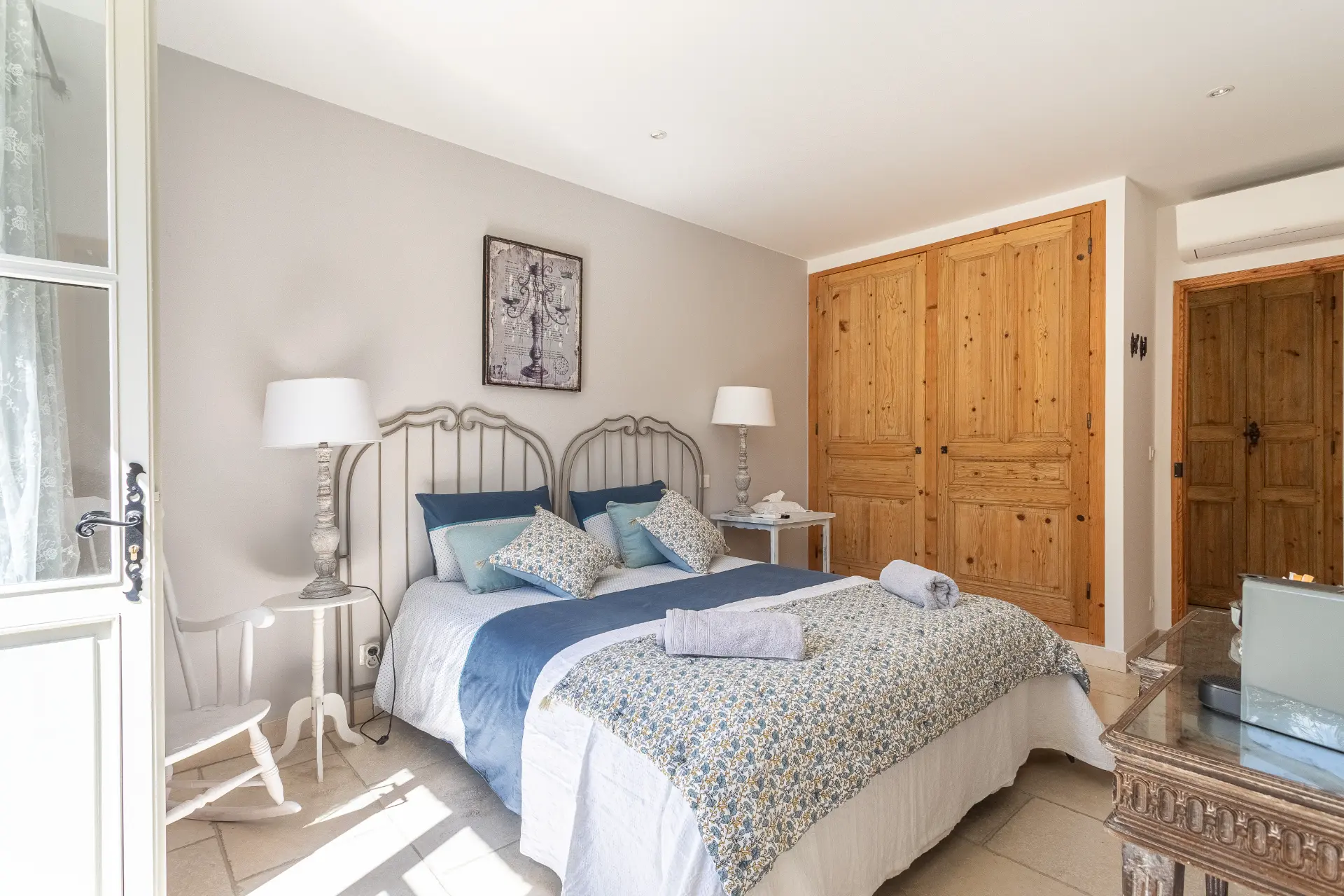 Chambre avec grand lit, plaid bleu, coussins et porte-fenêtre ouverte sur la terrasse