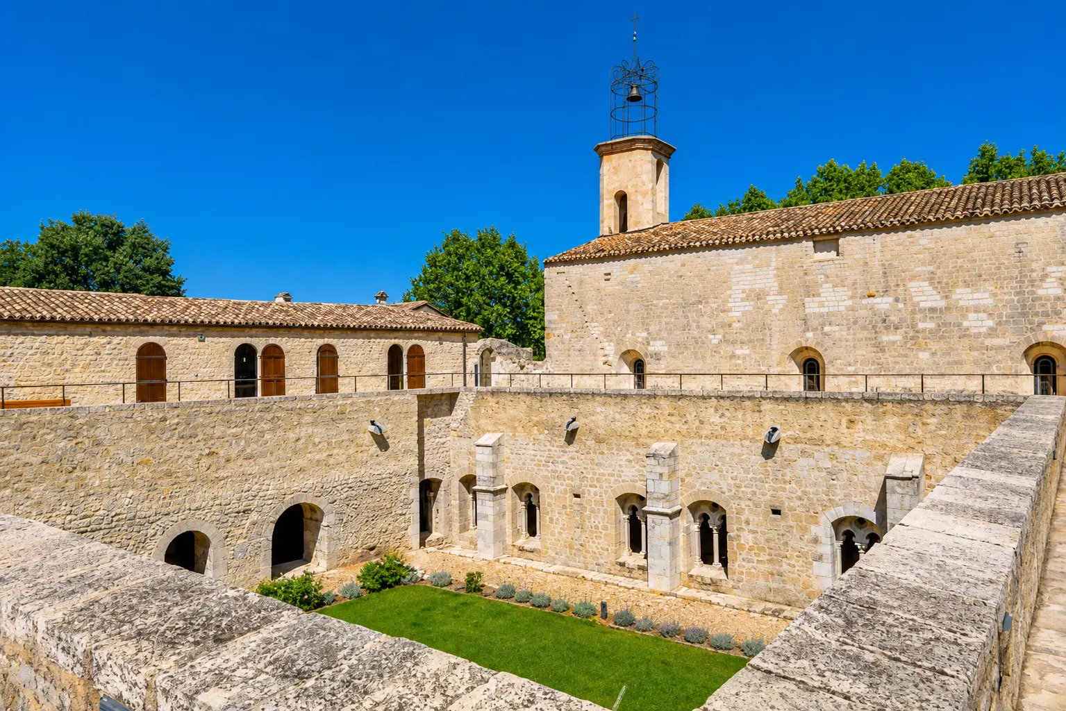 Abbaye cistercienne en pierre avec clocher, cloître et pelouse sous un ciel bleu