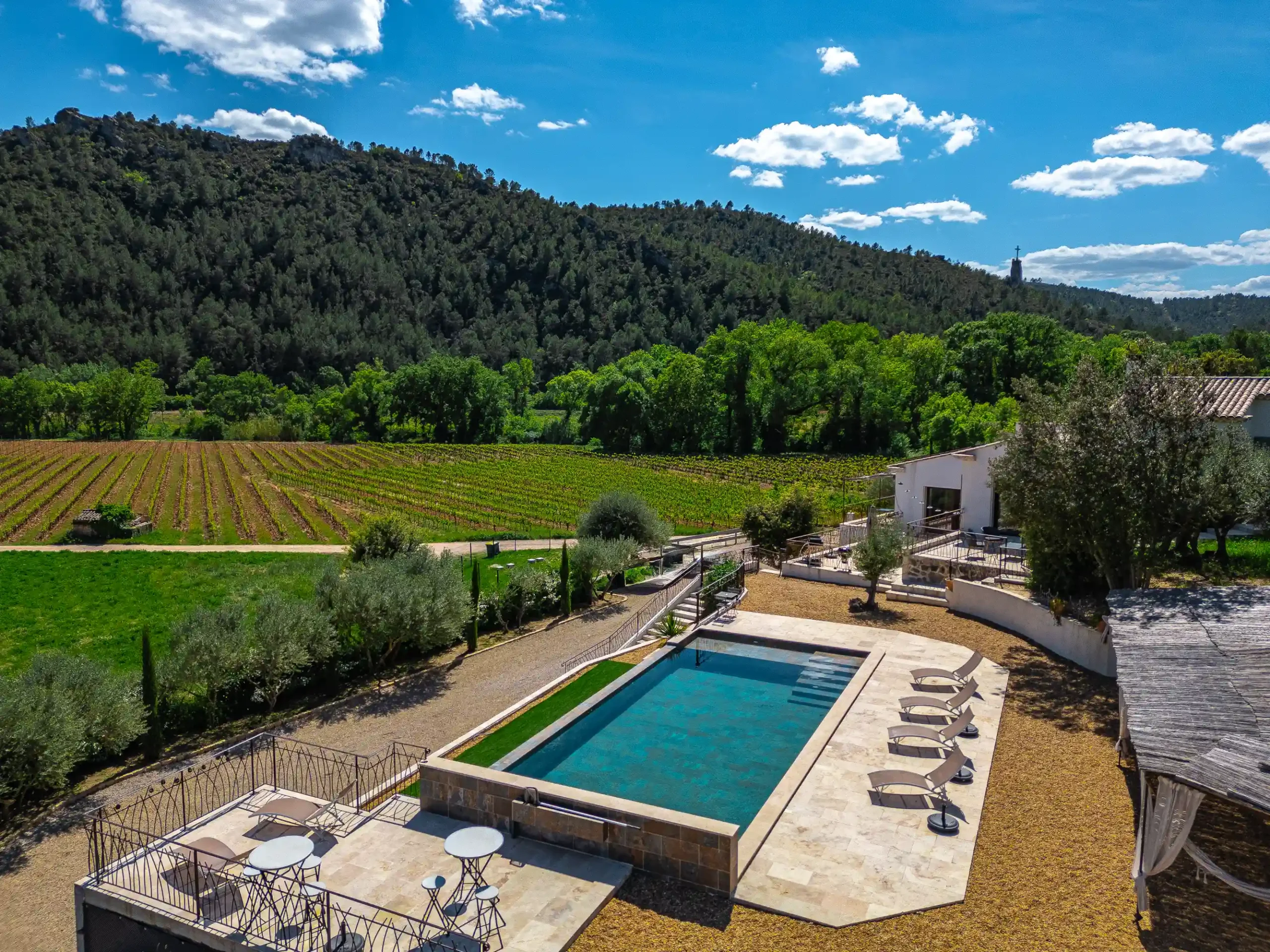 Piscine, transats et terrasses vus du ciel avec vignobles et collines boisées