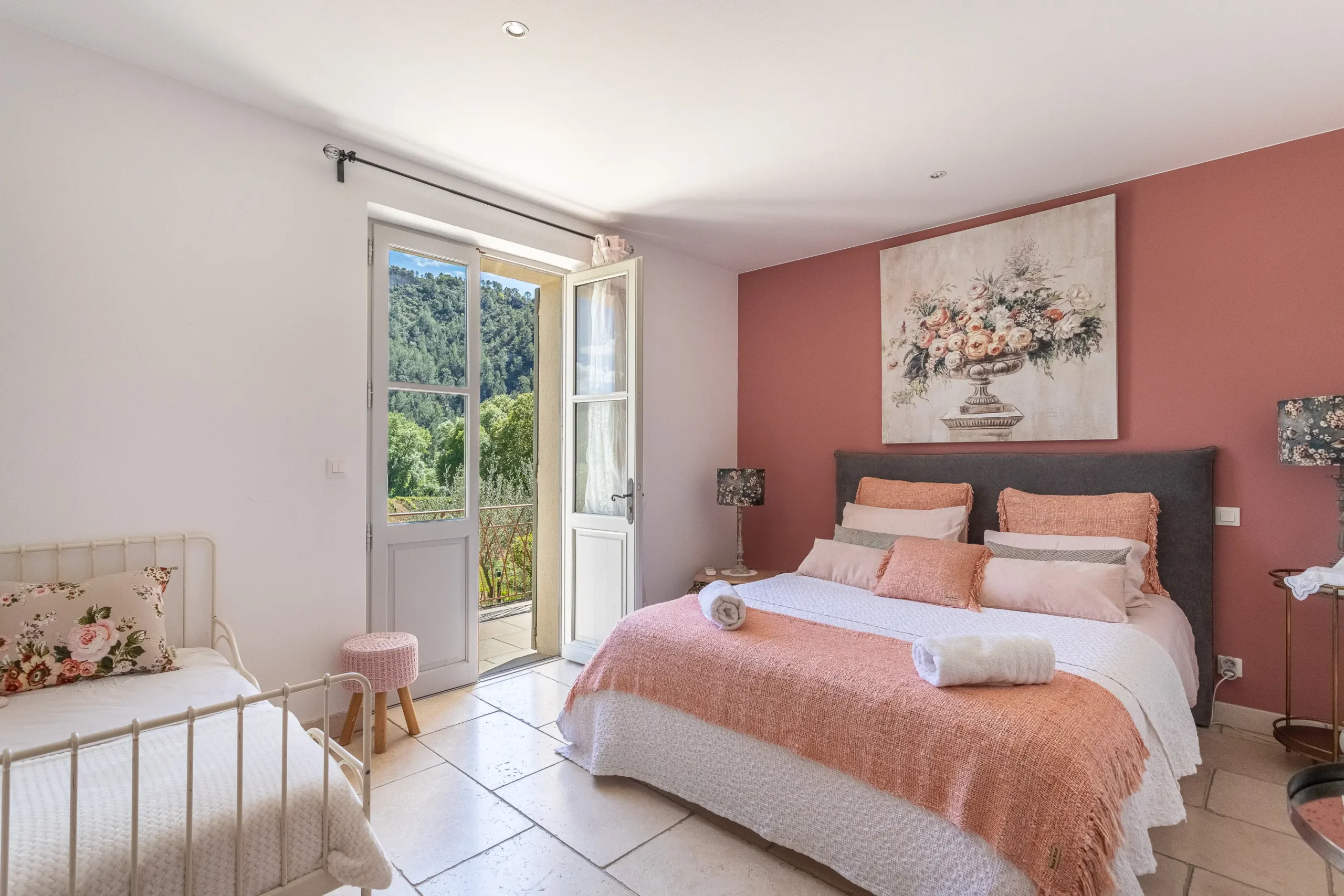 Chambre aux murs terracotta avec grand lit, coussins fleuris et porte-fenêtre ouverte