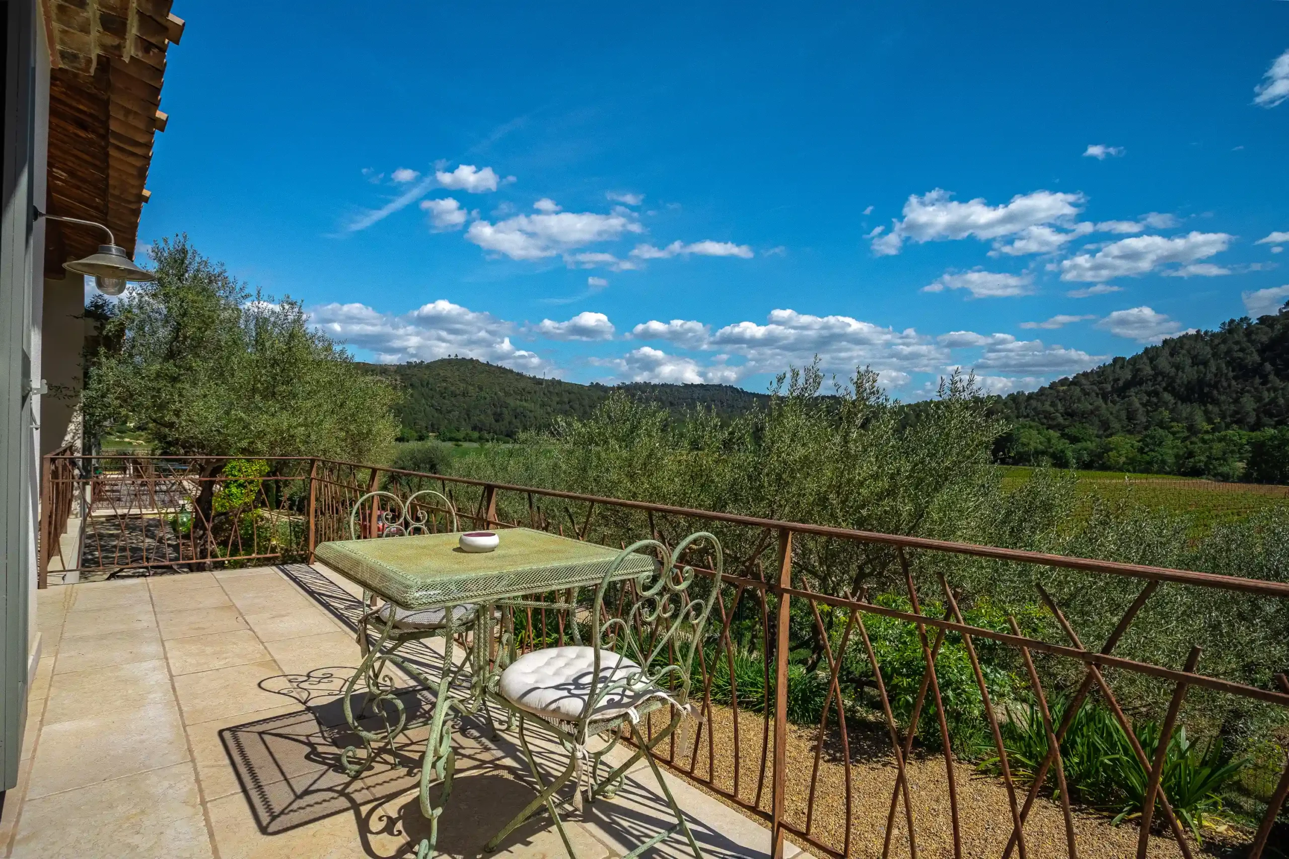 Terrasse carrelée avec petite table en fer forgé et vue sur les vignobles et collines