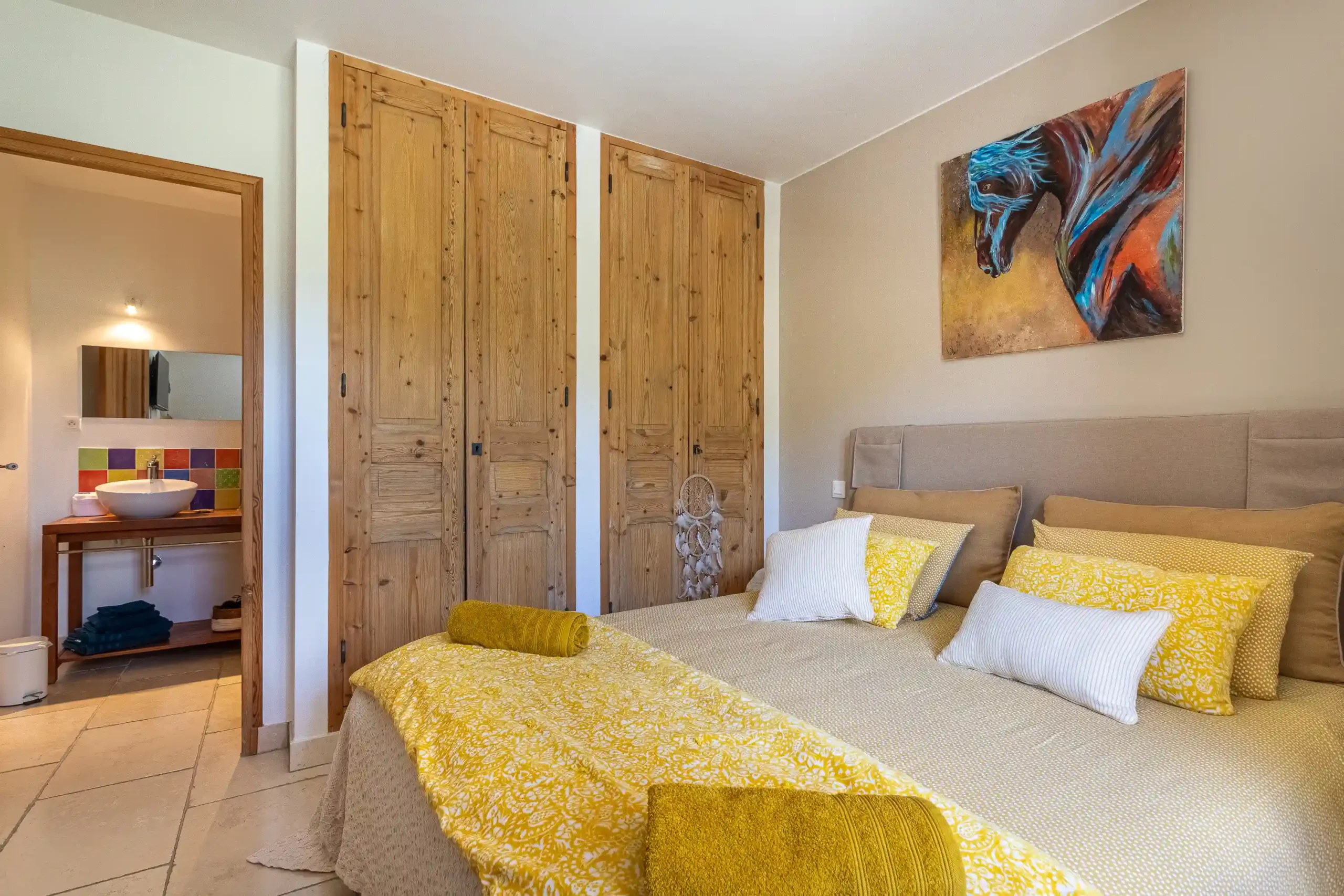 Chambre avec lit au couvre-lit doré, tableau de cheval et salle de bain colorée ouverte