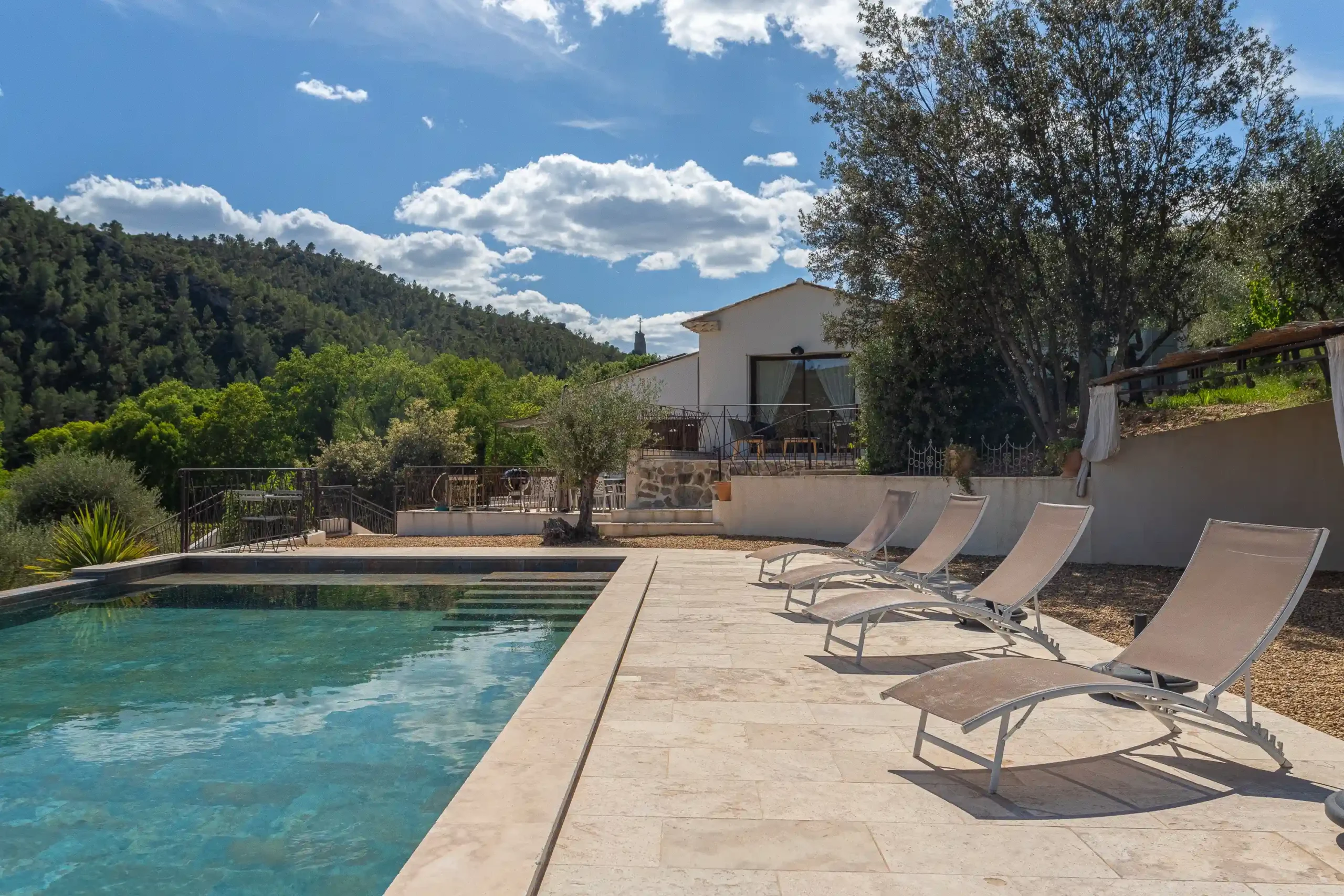 Piscine turquoise avec quatre transats sur pierre, villa et collines verdoyantes