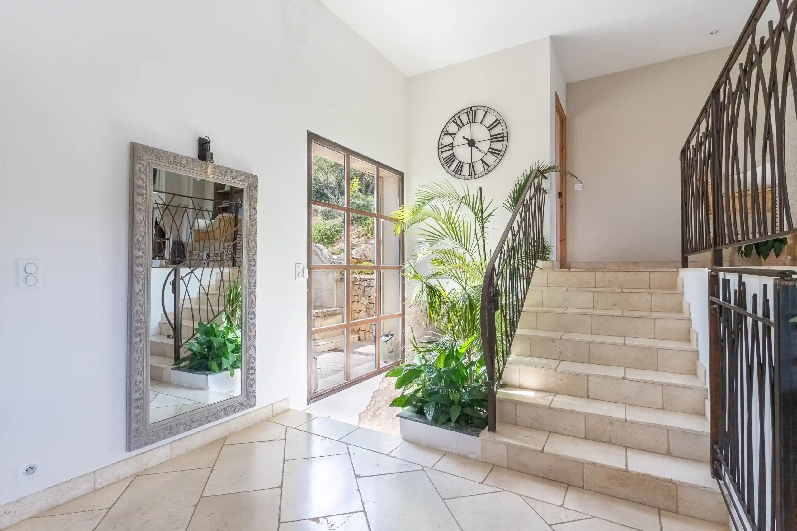 Escalier en pierre avec rampe en fer forgé, grande horloge et miroir dans l'entrée