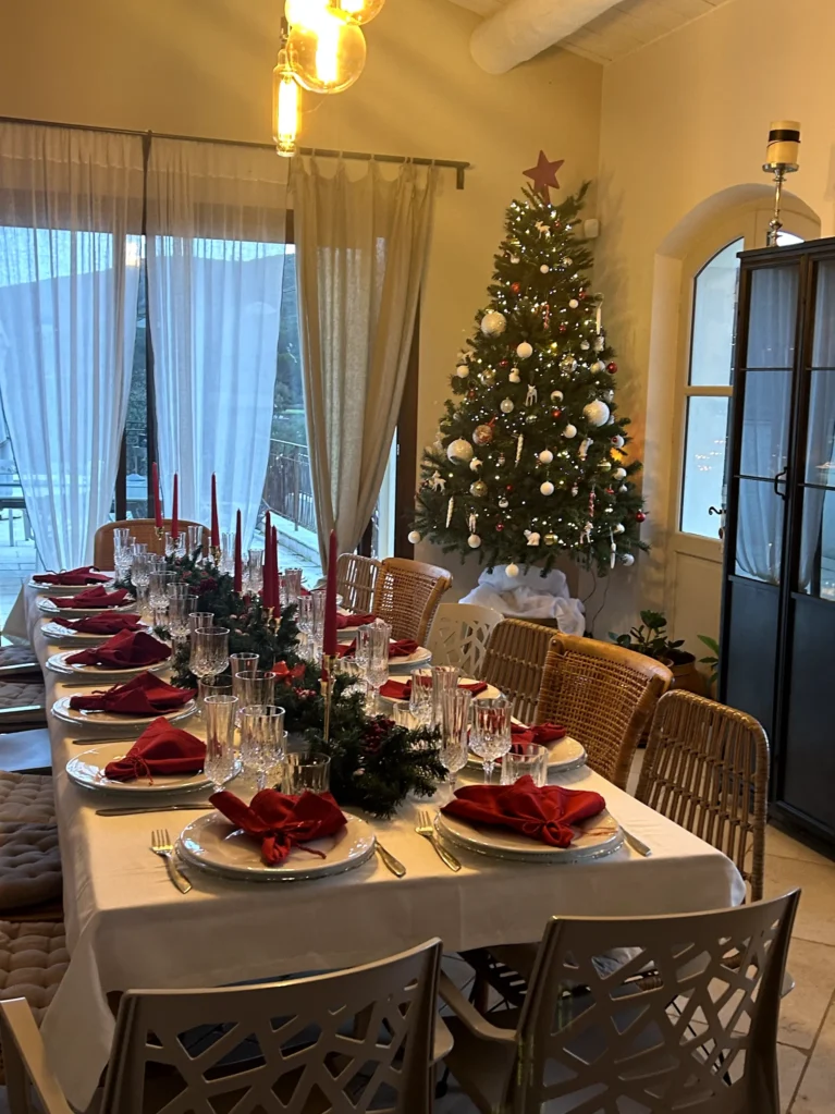 Table de Noël illuminée avec serviettes rouges et sapin décoré près des fenêtres