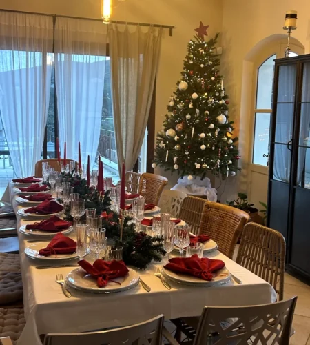 Table de Noël illuminée avec serviettes rouges et sapin décoré près des fenêtres