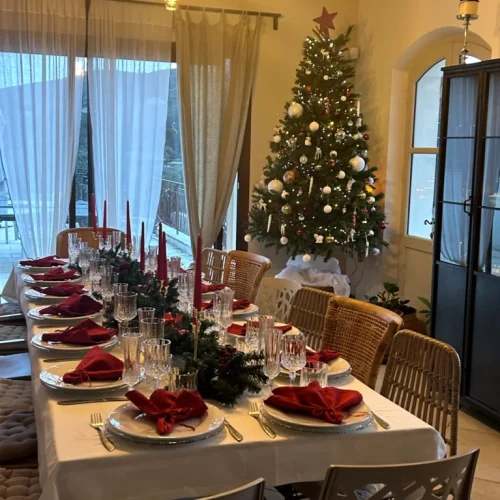 Table de Noël illuminée avec serviettes rouges et sapin décoré près des fenêtres
