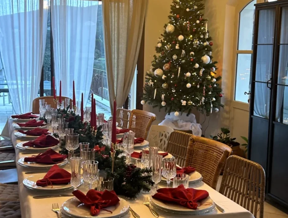 Table de Noël illuminée avec serviettes rouges et sapin décoré près des fenêtres