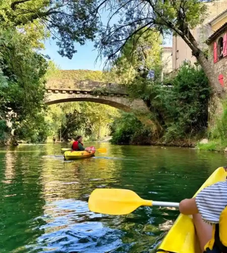 Enfant en kayak jaune sur la rivière Argens avec pont en pierre et maisons