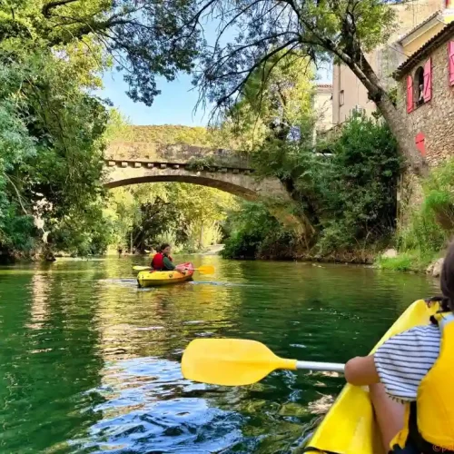 Enfant en kayak jaune sur la rivière Argens avec pont en pierre et maisons
