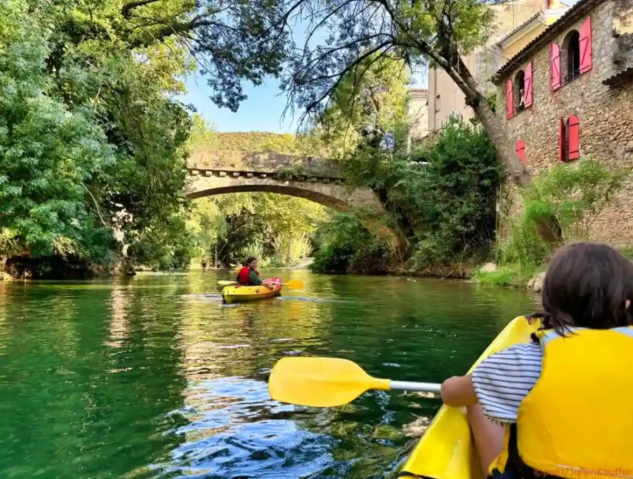 Enfant en kayak jaune sur la rivière Argens avec pont en pierre et maisons